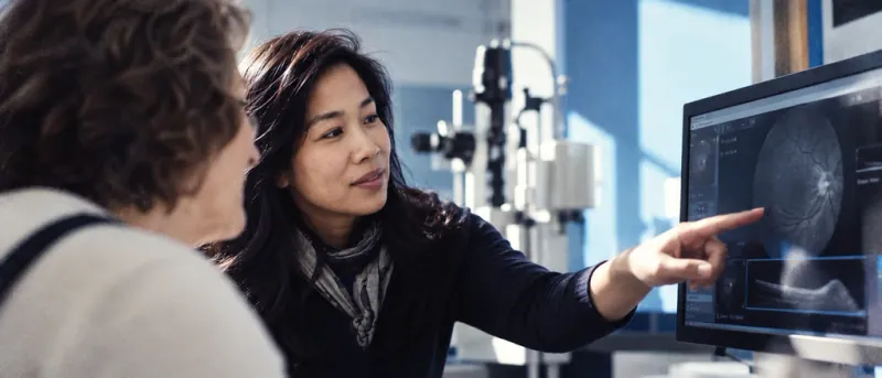 Optometrist explaining a retinal scan on a monitor to a seated patient
